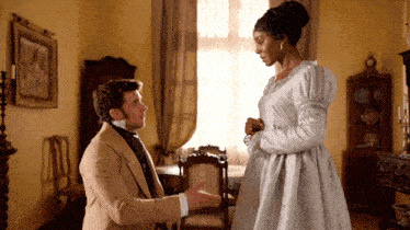 a man in a tan suit is kneeling down to a woman in a white dress