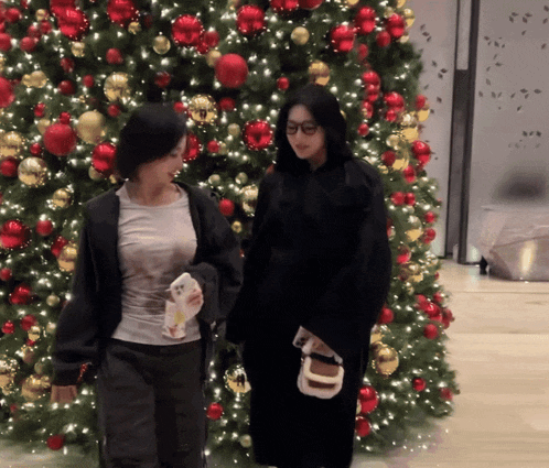 two women standing in front of a christmas tree holding hands