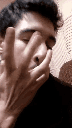a young man is covering his face with his hand while smoking a cigarette .