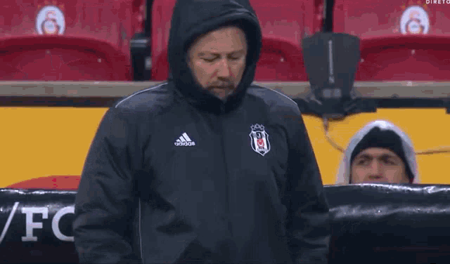 a man wearing an adidas jacket is standing in a stadium
