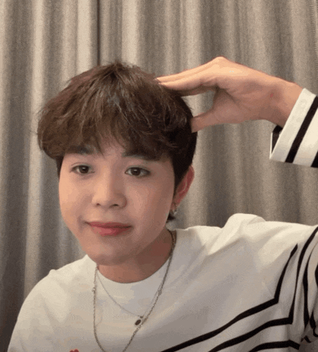 a young man wearing a striped shirt has his hand on his forehead