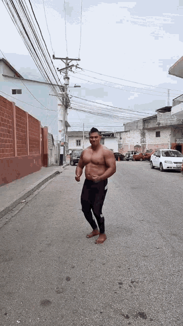 a man without a shirt is walking down a street with cars parked behind him