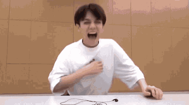 a young man in a white shirt is sitting at a table with headphones on it