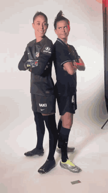 two female soccer players standing back to back with their arms crossed