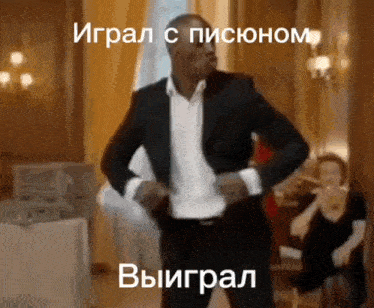 a man in a suit and white shirt is dancing in a room with a woman sitting in the background