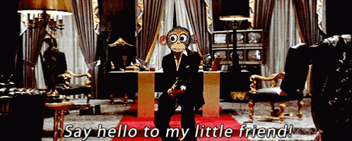 a man in a suit with a monkey mask on his face is standing in a room and saying " say hello to my little friend "