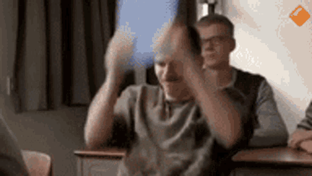 a man is sitting at a desk in a classroom with his hands up in the air .