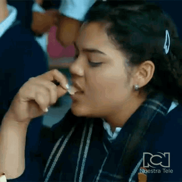 a girl in a school uniform is eating a piece of food from her hand .