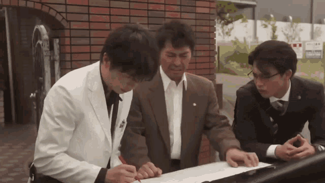 a man in a white coat is writing on a piece of paper in front of two other men