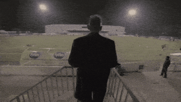 a man in a suit stands on stairs looking at a soccer field with a sign that says tylies