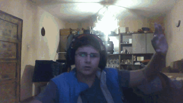 a man wearing headphones and a blue vest holds up his hand