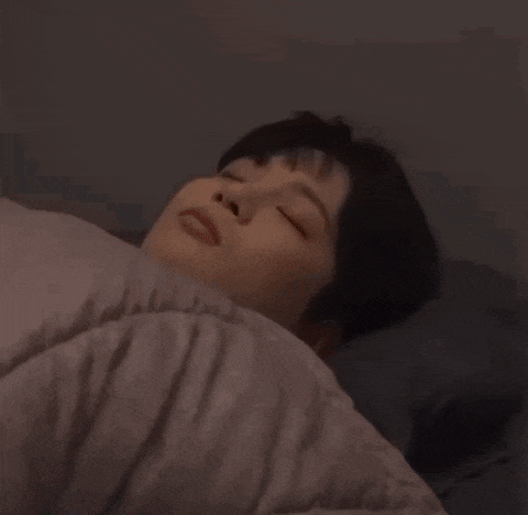a man is sleeping in a bed with his eyes closed and a blanket .