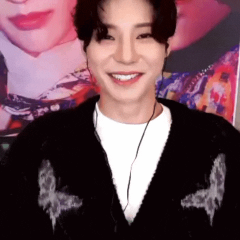 a young man wearing a black sweater and headphones is smiling in front of a picture of a man .