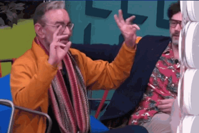 a man in an orange jacket and scarf is making a gesture