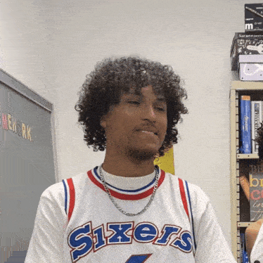 a man wearing a sixers jersey stands in front of a blackboard