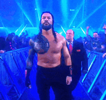 a shirtless wrestler with a shield on his chest walks through a tunnel