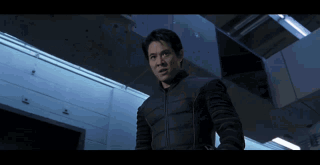 a man in a black jacket stands in a room