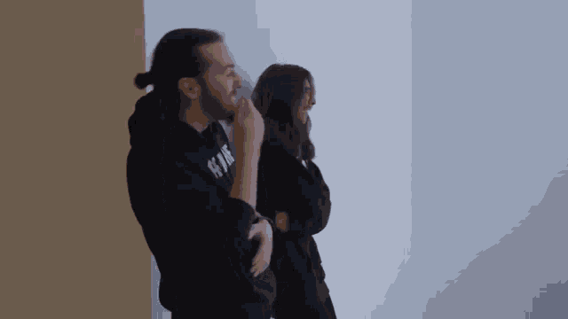a man and a woman are standing next to each other and the man is wearing a hoodie that says ' a '