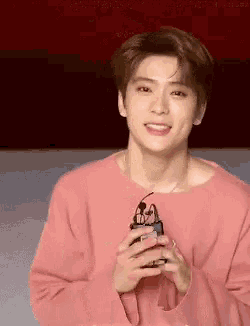 a young man in a pink sweater is smiling and holding a pair of glasses .