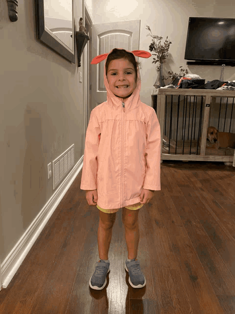 a little girl wearing a pink raincoat with bunny ears on her head