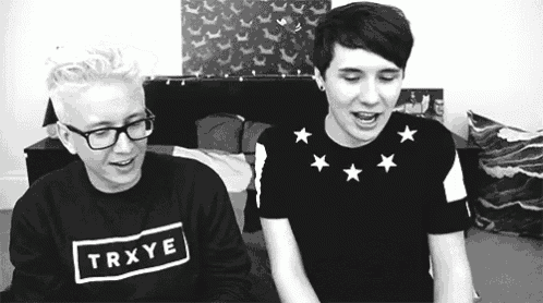 a black and white photo of two young men sitting next to each other . one of the men is wearing a trxye shirt .