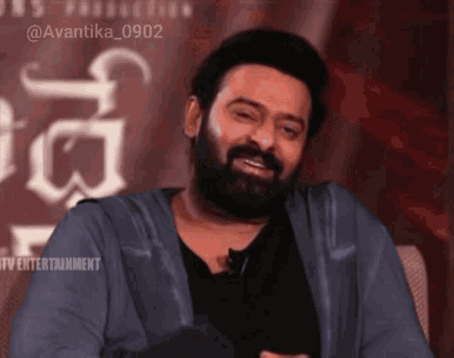 a man with a beard is sitting in front of a sign that says avantika 0902