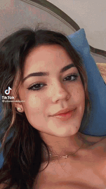 a woman is laying on a bed with a blue pillow and a tiktok icon on her face