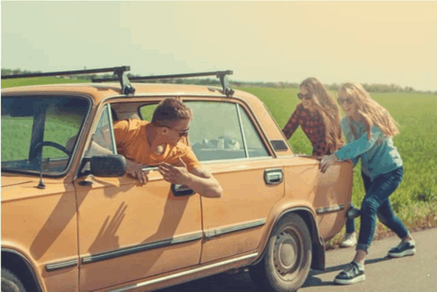 a man leaning out of a car window while two girls push the car