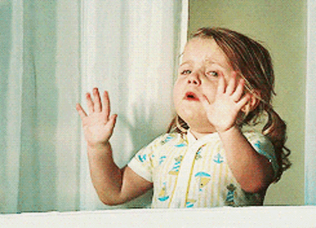 a little girl looking out a window with her hands on the glass