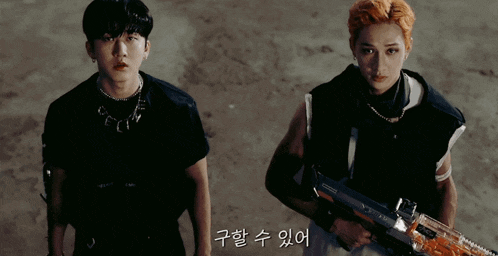 two young men standing next to each other with one holding a rifle