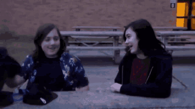 two girls are sitting at a picnic table in front of a building with a sign that says no smoking