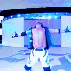a shirtless wrestler with his arms outstretched in front of a large screen
