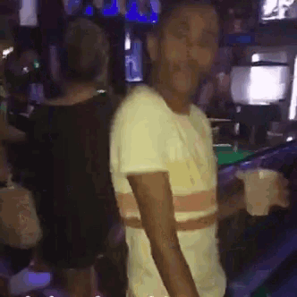 a man in a white shirt is dancing in a dark room while holding a drink .