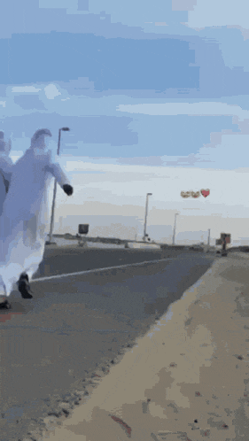 a man in a white robe walks down a road