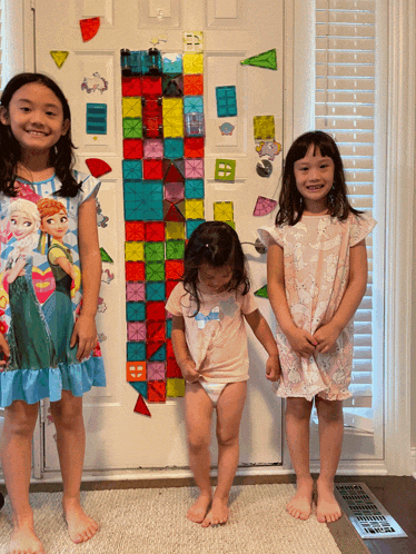 three little girls are standing in front of a door with a frozen theme