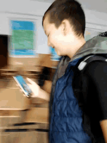a boy in a blue vest holds a cell phone