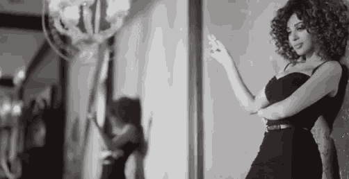 a woman in a black dress is standing in front of a mirror in a black and white photo .