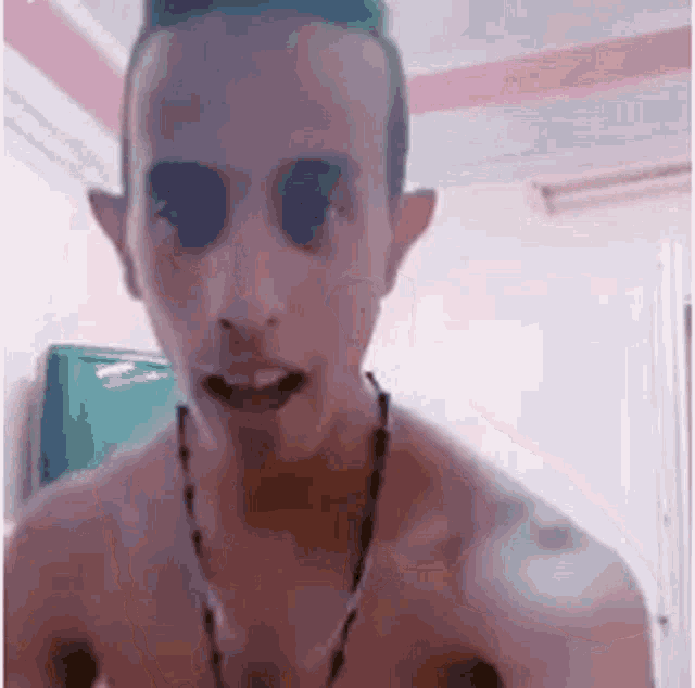 a man without a shirt is wearing a necklace and looking at the camera .