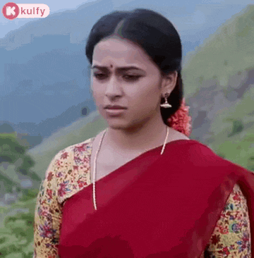 a woman in a red saree and a yellow blouse is standing in front of a mountain .