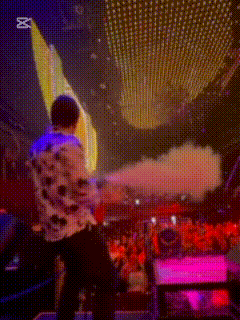 a man in a floral shirt is standing in front of a crowd holding a yellow flag