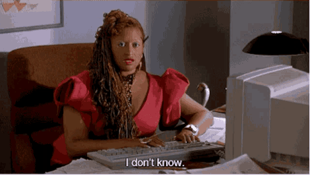 a woman in a pink dress is sitting at a desk in front of a computer and says i don 't know .