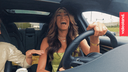 a woman is driving a car with videoland written on the dashboard