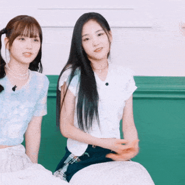 two girls are sitting next to each other on a green wall
