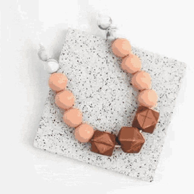a necklace with peach and brown beads is sitting on top of a white tray .