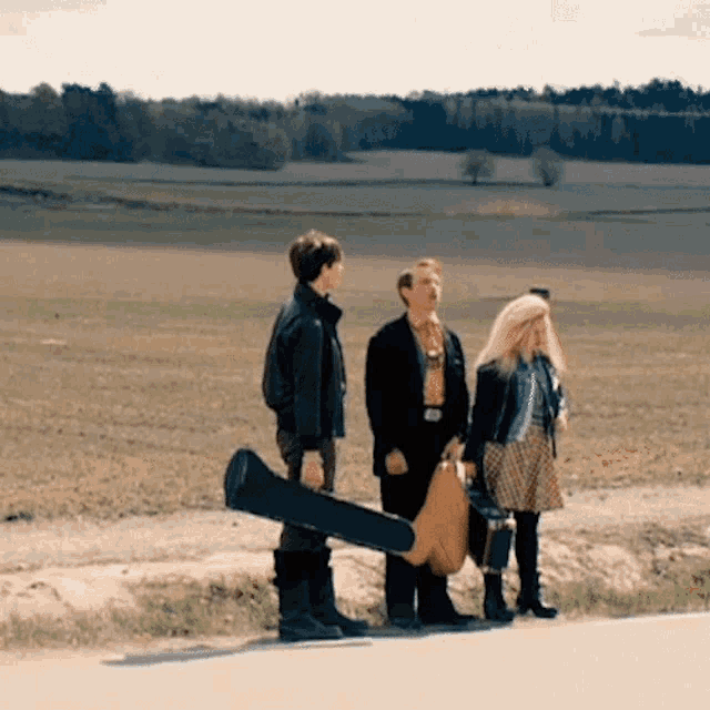 a man carrying a guitar case is standing next to two other people