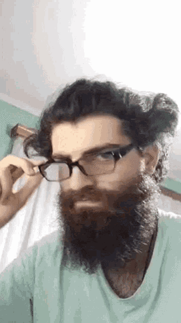 a man with a beard wearing glasses and a green shirt .