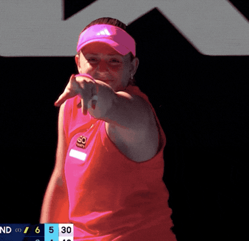 a woman wearing a pink visor and a pink tank top points at the camera