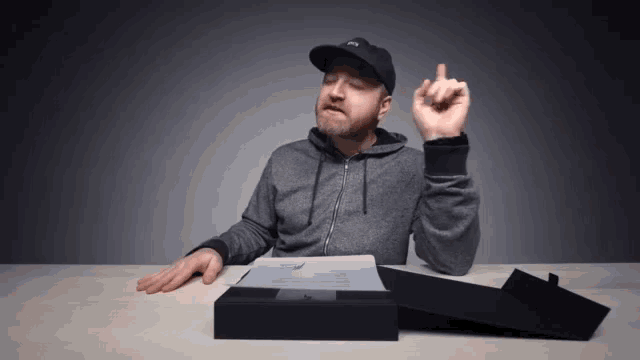 a man wearing a hat and a hoodie is sitting at a table