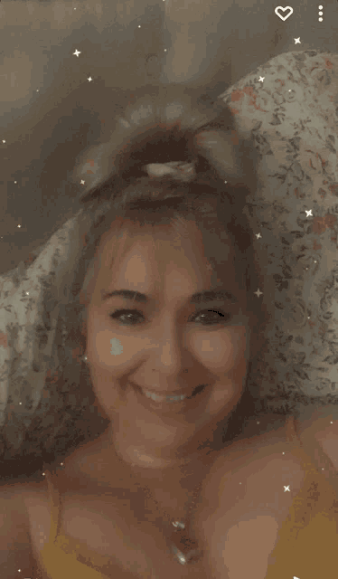 a woman in a yellow top smiles while laying in bed