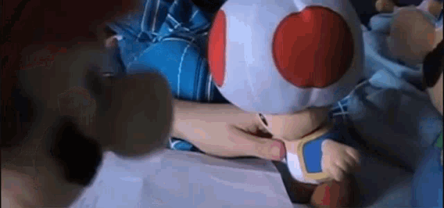 a person is holding a stuffed toad with a red and white hat on a bed .